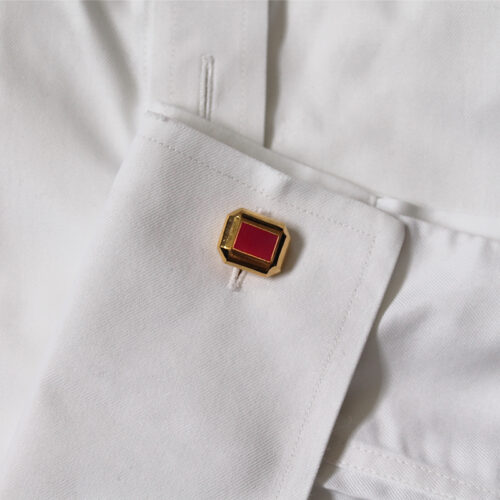 Gold cufflink with red enamel on shirt cuff